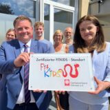 Caritas-Mitarbeiter und Bürgermeister zeigen „Fitkids“-Siegel.