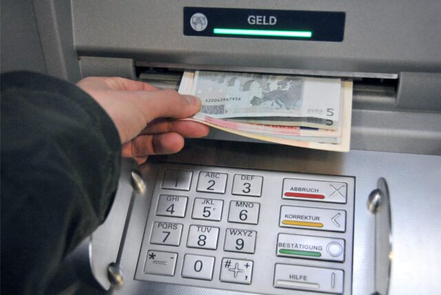 Eine Hand greift nach Geld aus einem Geldautomaten