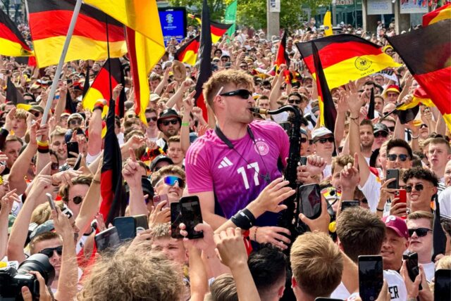 Saxophonist André Schnura spielt während der EM 2024 inmitten von Fans auf dem Friedensplatz in Dortmund.