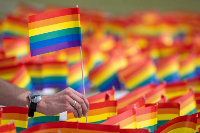 Ein Mann hält ein Regenbogenfähnchen in der Hand.