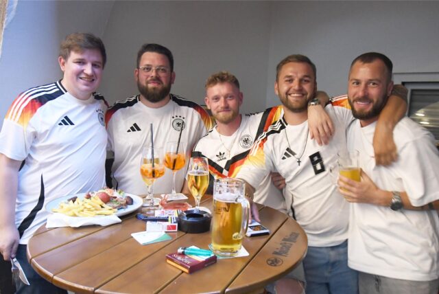 Fünf Männer in Deutschland-Trikot stehen an einem Tisch mit Getränken und etwas zu essen.