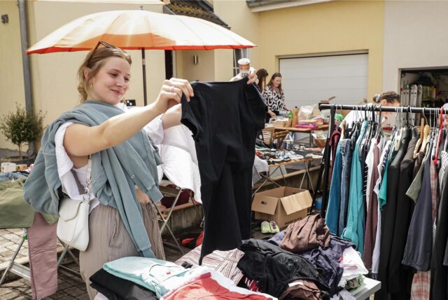 Eine junge Frau stöbert Kleidungsstücke auf einem Flohmarkt in Dortmund durch.