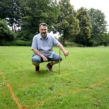 Stefan Seifert, Pressesprecher des BGV Backumer Tal, hockt auf der Wiese vor dem Vereinsgelände neben einer Markierung.