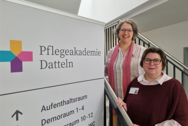 Kathrin Volz und Heike Beughold stehen vor einem Plakat.