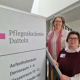 Kathrin Volz und Heike Beughold stehen vor einem Plakat.