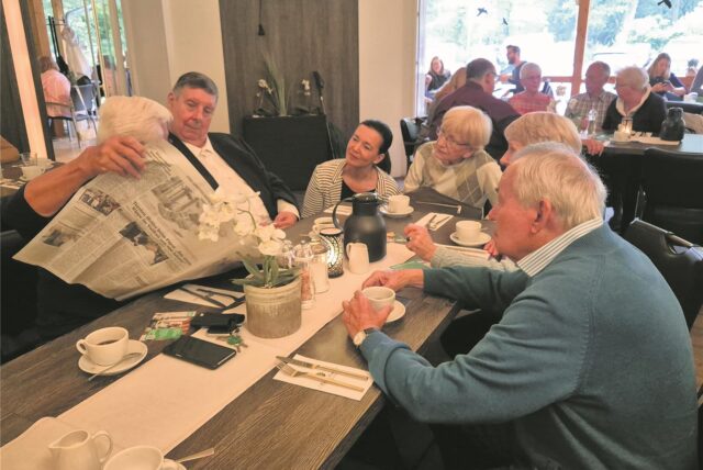 Menschen sitzen an einem Tisch und schauen in eine Zeitung.