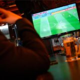 Ein Mann sitzt an der Bar in und schaut auf einem Fernseher Fußball.