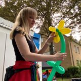 Stelzenläuferin „Phoenix Mia“ hat aus Luftballons eine Blume gestaltet.