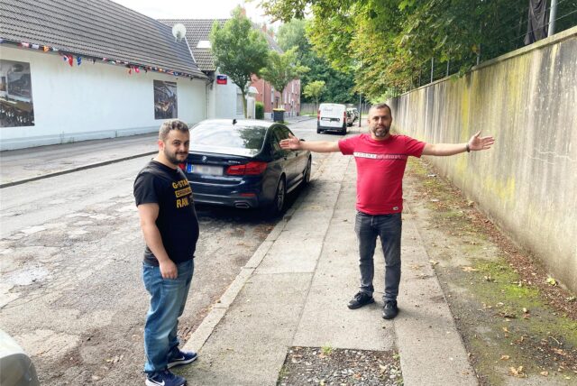 Zwei Männer stehen auf einem Bürgersteig, einer breitet die Arme aus, um zu zeigen, wie viel Platz der Bürgersteig bietet.