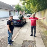 Zwei Männer stehen auf einem Bürgersteig, einer breitet die Arme aus, um zu zeigen, wie viel Platz der Bürgersteig bietet.