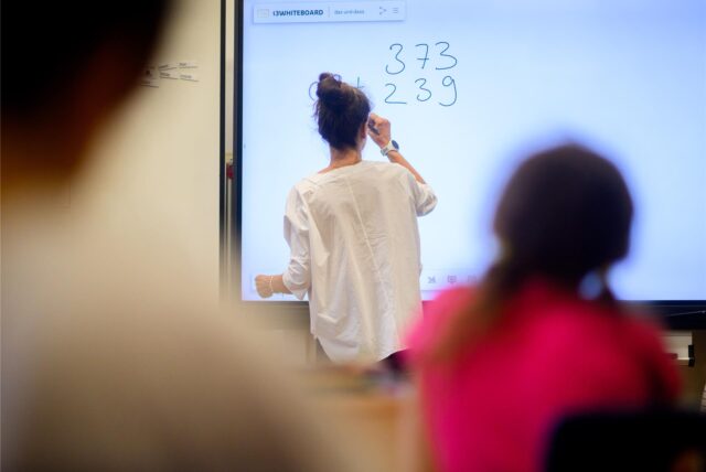 Eine Lehrerin schreibt eine Rechenaufgabe an ein Whiteboard.