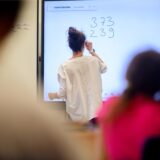 Eine Lehrerin schreibt eine Rechenaufgabe an ein Whiteboard.