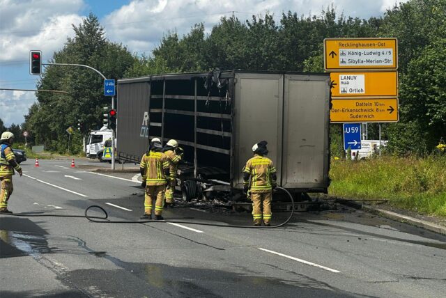 Feuerwehrleute stehen vor einem ausgebrannten Lkw-Anhänger.