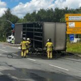 Feuerwehrleute stehen vor einem ausgebrannten Lkw-Anhänger.