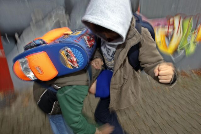 Zwei Jungen mit Schultaschen auf dem Rücken kämpfen miteinander. (Symbolbild)