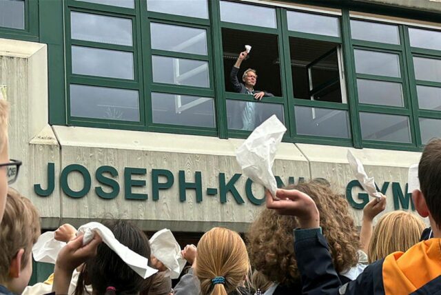 Schulleiter Ulrich Wessel steht am Fenster und schaut auf eine Menge aus Schülern hinunter