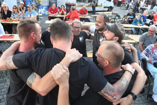 Impression bei der Castropiade 2023 auf dem Marktplatz in Castrop:Teamteilnehmer stehen Arm in Arm im Kreis.