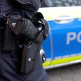 Die Waffe eines Polizisten in einer Halterung, dahinter ein Polizeiauto.