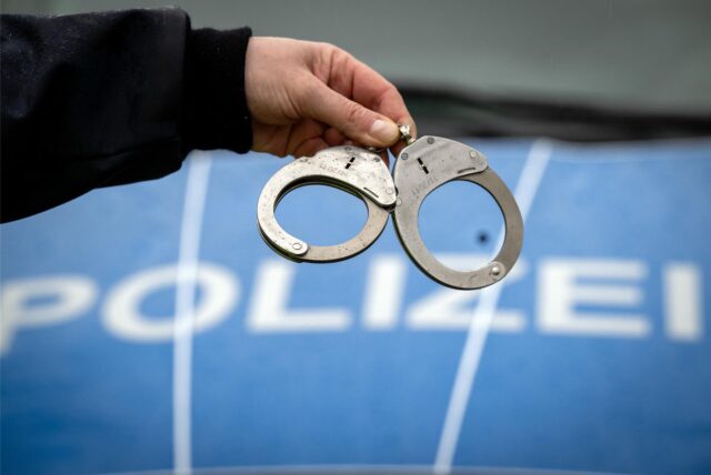 Ein Polizist hält ein Paar Handschellen. (Symbolbild)