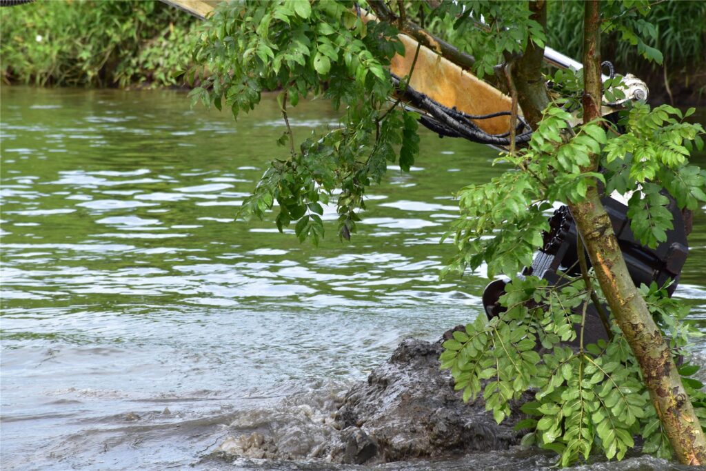 Ein Schwimmbagger gräbt auf der Lippe am Ufer.