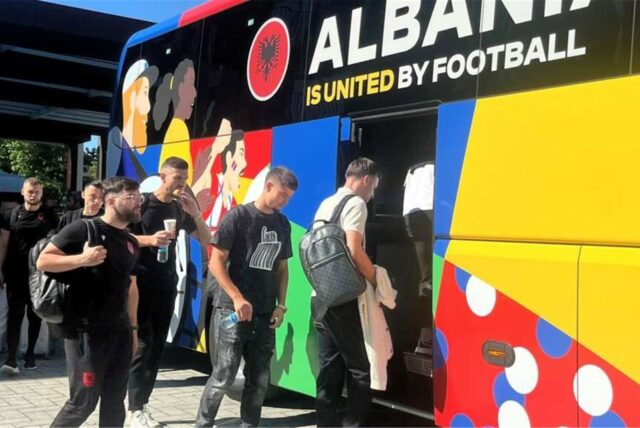 Mehrere Fußballspieler besteigen einen Bus mit der Aufschrift „Albany is united by football“ (Albanien wird durch den Fußball vereint).