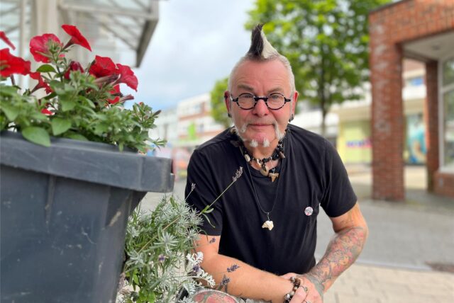 Punky Bahr hockt neben einer grauen, mit roten Blumen bepflanzten Tonne.