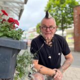 Punky Bahr hockt neben einer grauen, mit roten Blumen bepflanzten Tonne.