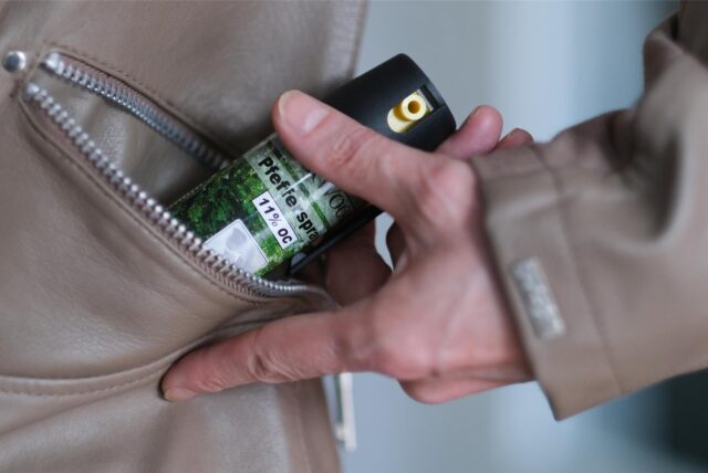 Eine Hand greift nach einer Pfefferspray-Flasche in einer Jackentasche.