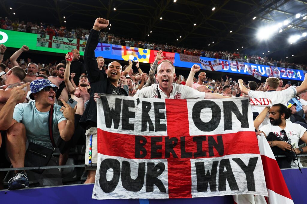 Englische Fans feiern den Einzug ihrer Nationalmannschaft ins Finale der Fußball-Europameisterschaft 2024. Die Flagge, die der Fan in die Kamera hält, trägt den Schriftzug 