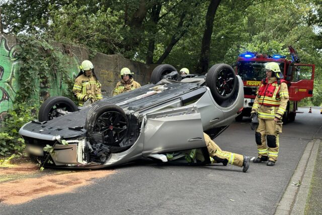 Nach einem schweren Unfall liegt ein Auto auf dem Dach. Einsatzkräfte der Feuerwehr stehen um das Auto herum.