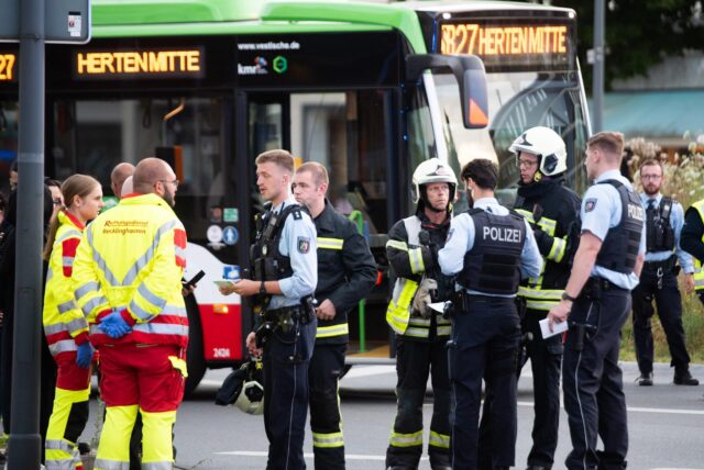 Rettungskräfte und Polizisten stehen auf einer Straße, im Hintergrund ein Linienbus.