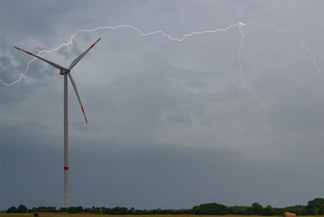 Ein Windrad steht vor einem grauen Himmel. Ein Blitz zuckt über den Horizont.