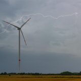 Ein Windrad steht vor einem grauen Himmel. Ein Blitz zuckt über den Horizont.
