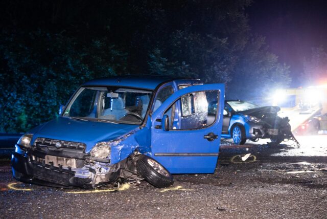 Ein blauer Transporter steht schwer demoliert auf der Straße. Im Hintergrund steht ein weiteres Unfallauto.