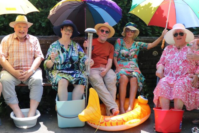 Seniorinnen und Senioren aus Recklinghausen sitzen unter Sonnenschirmen und kühlen ihre Füße in kleinen Wasserbecken.