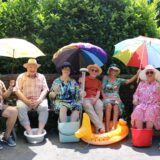 Seniorinnen und Senioren aus Recklinghausen sitzen unter Sonnenschirmen und kühlen ihre Füße in kleinen Wasserbecken.