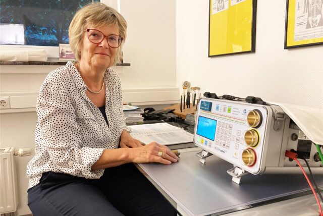 Heike Karwasz sitzt in einem Behandlungszimmer an einem Tisch mit einem elektronischen Messgerät.