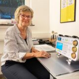 Heike Karwasz sitzt in einem Behandlungszimmer an einem Tisch mit einem elektronischen Messgerät.