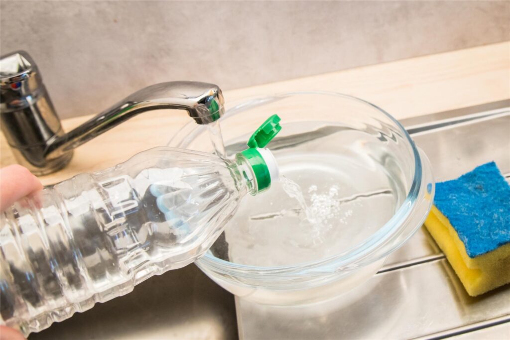 Eine Wasserschale, in die Wasser und Essig gefüllt werden, um den Kühlschrank zu reinigen. Daneben ein Kühlschrank. Eine Wasserschale, in die Wasser und Essig gefüllt werden, um den Kühlschrank zu reinigen. Daneben ein Kühlschrank.