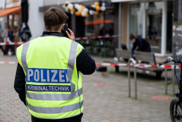 Ein Polizist tragt eine gelbe Warnweste mit dem Aufdruck „Polizei Kriminaltechnik“ und telefoniert.
