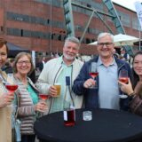 Drei Frauen und zwei Männer stehen auf dem Gelände der Zeche Ewald in Herten-Süd an einem Tisch, halten jeweils ein Glas Wein bzw. Bier in einer Hand.