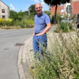 Ein Mann steht mit Jeans und blauem Polohemd an einem Straßenrand in Recklinghausen und zeigt mit einer Handbewegung den hochgewachsenen Grünstreifen.