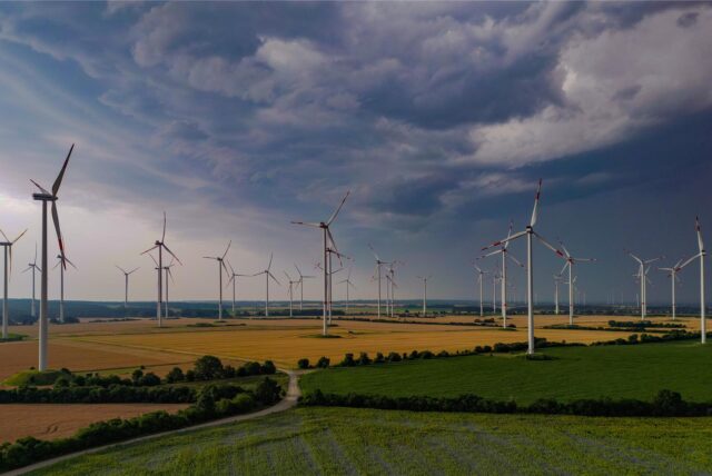 Dunkle Wolken einen nahenden Gewitters ziehen am frühen Morgen über die Landschaft mit einem Windenergiepark im Osten von Brandenburg