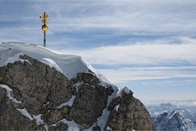 Schneebedeckter Berggipfel mit einem goldenen Kreuz.