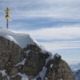 Schneebedeckter Berggipfel mit einem goldenen Kreuz.