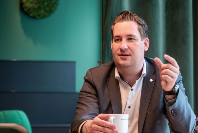 Brian Nickholz, Stadtverbandsvorsitzender der Marler SPD, sitzt an einem Tisch und hält eine Tasse Kaffee in der Hand. Mit der anderen Hand gestikuliert er.
