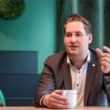 Brian Nickholz, Stadtverbandsvorsitzender der Marler SPD, sitzt an einem Tisch und hält eine Tasse Kaffee in der Hand. Mit der anderen Hand gestikuliert er.