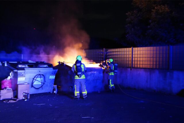 Feuerwehrleute löschen einen brennenden Container auf einem Sammelplatz.