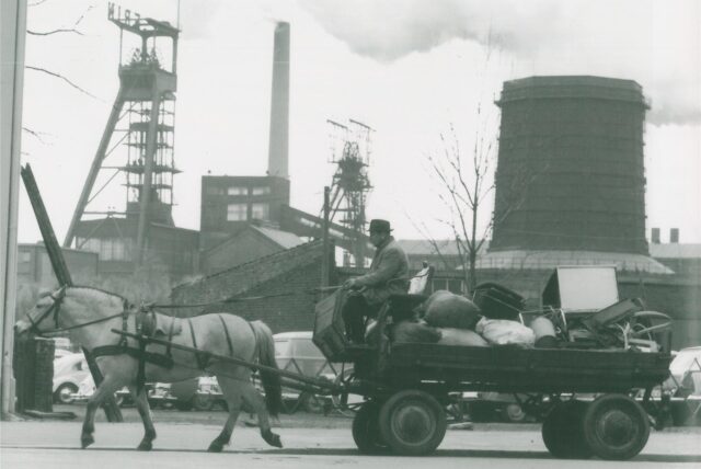 Ein Altwarenhändler mit Pferdefuhrwerk vor der Kulisse der Zeche Erin in Castrop-Rauxel.