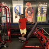 Ein Mann im roten T-Shirt steht in einem Fitness-Studio zwischen den Geräten.